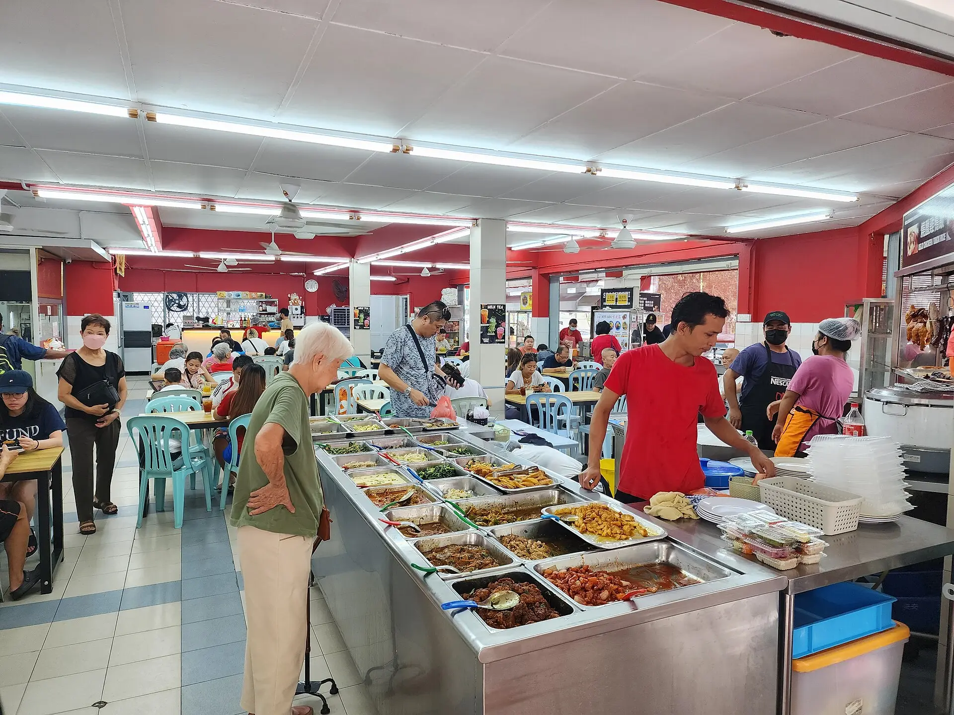 热闹的马来西亚咖啡店，柜台上摆满咖喱和小炒，食客坐在简单的桌前用餐